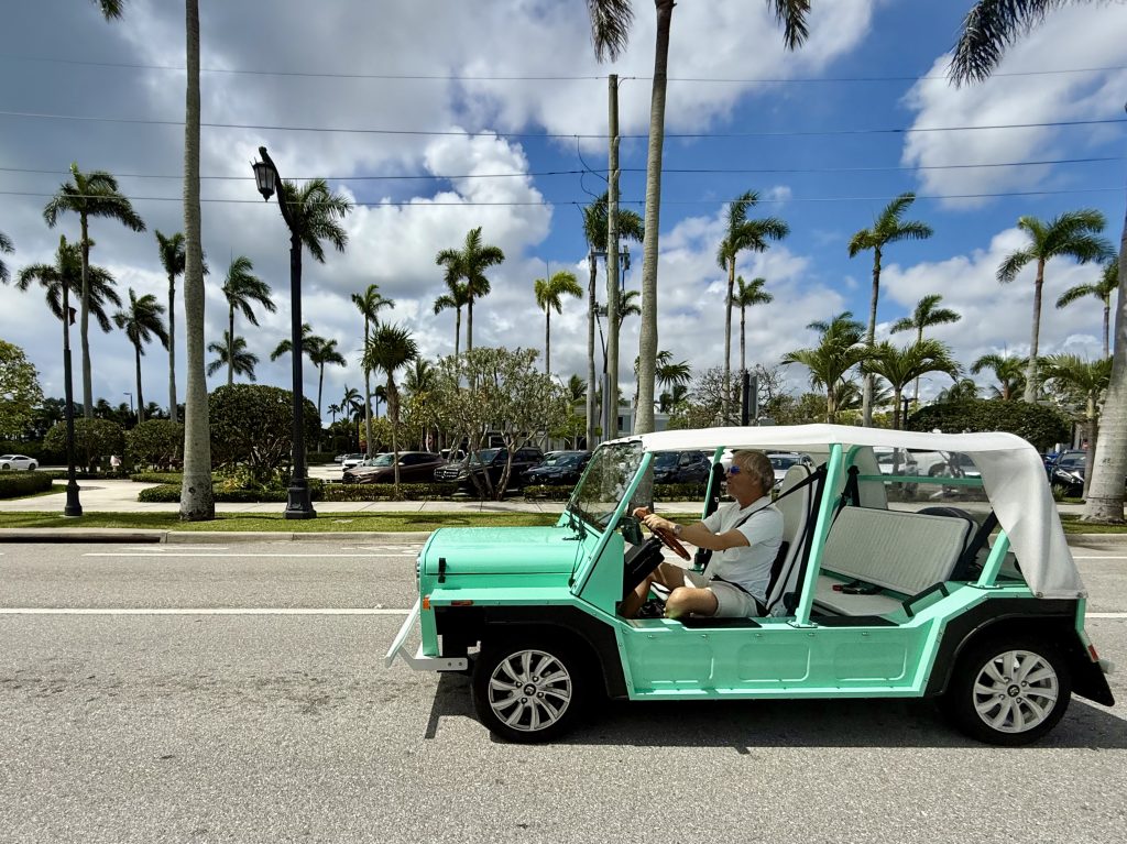 Moke electric car driving through palm-lined streets in Florida, perfect for enclosed shipping along the East Coast.
