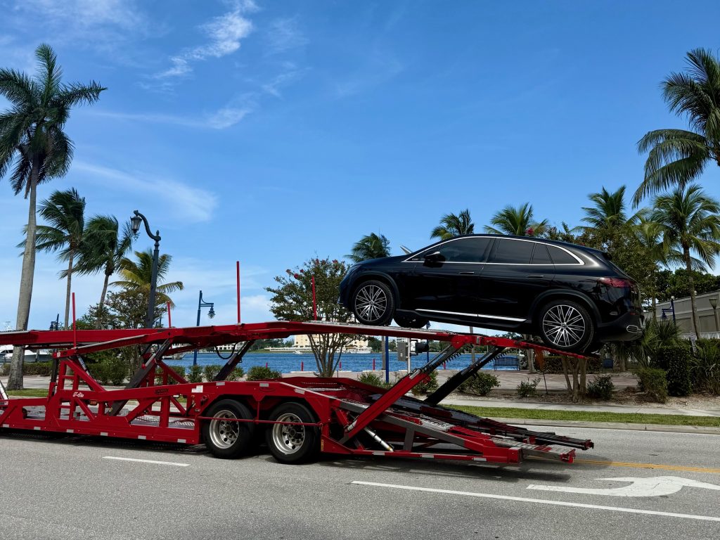 Black SUV secured on the upper deck of a red car hauler heading to The Villages, Florida.