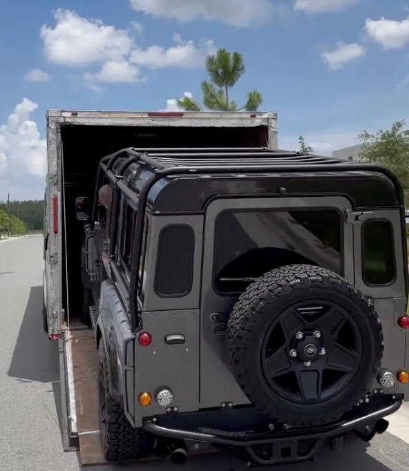 Custom black Land Rover Defender 90 being loaded into an enclosed auto transport trailer