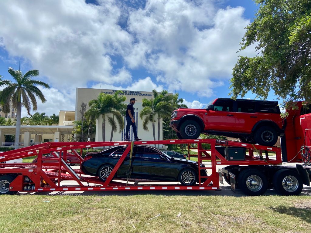 Red Ford Bronco and black sedan transported on a red open car carrier to The Villages, Florida.